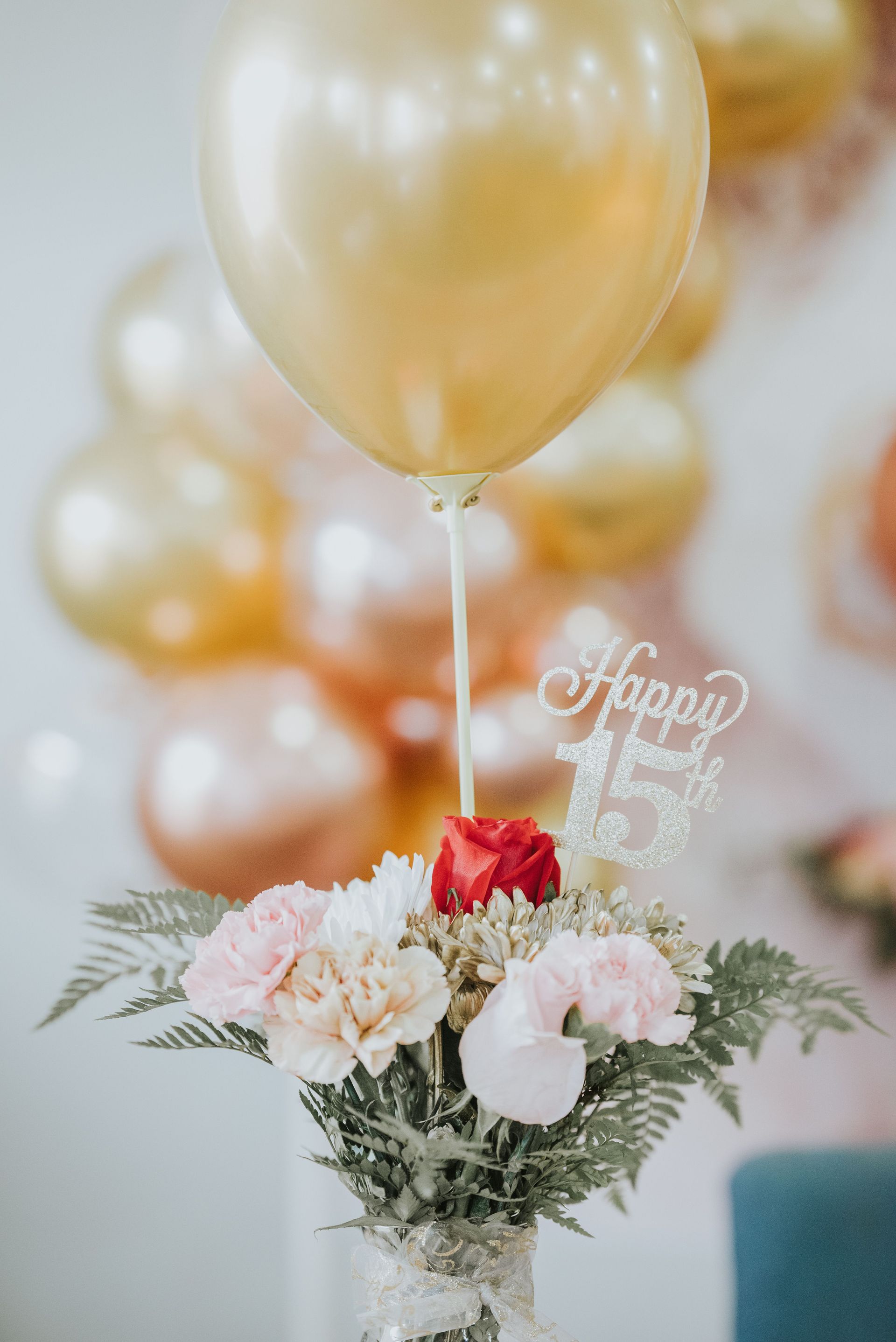 Beautiful floral arrangement with "Happy 15th" balloon for celebration.